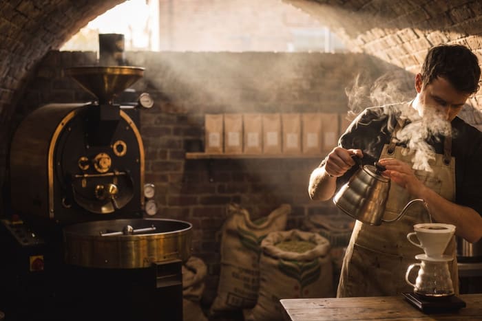 A roaster pouring a filter coffee in a railway arch, steam in the morning light